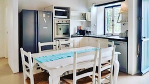 A compact kitchen with white cabinetry, a dining table with four chairs, a built-in oven, and a microwave. - 5 Bedroomed Fisherman's Cottage in Struis Bay (Struisbaai)