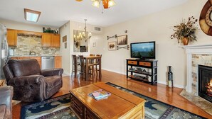 Un salon avec une cheminée, un ventilateur de plafond, un coin repas et une cuisine.