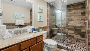 Une salle de bain équipée d’un lavabo, d’un miroir et de toilettes. Elle comprend également une douche avec une porte en verre et des carreaux de mur en bois.