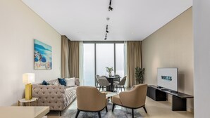 Ein modernes Hotelzimmer mit einem Bett, zwei Sesseln, einem Fernseher und einem Essbereich mit Tisch und Stühlen.