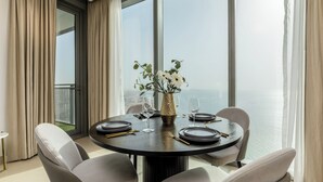 Ein runder Esstisch mit sechs Stühlen, eine Vase mit weißen Blumen und Meerblick durch große Fenster.