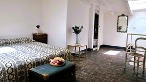 Een kamer met een bed, een klein tafeltje met een vaas, een stoel en een koffer.