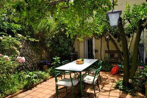 Un patio con mesa y sillas, rodeado de follaje y un muro de piedra.