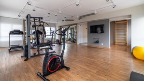 Un gimnasio amplio con diversos equipos de ejercicio, suelo de madera y un espejo grande.