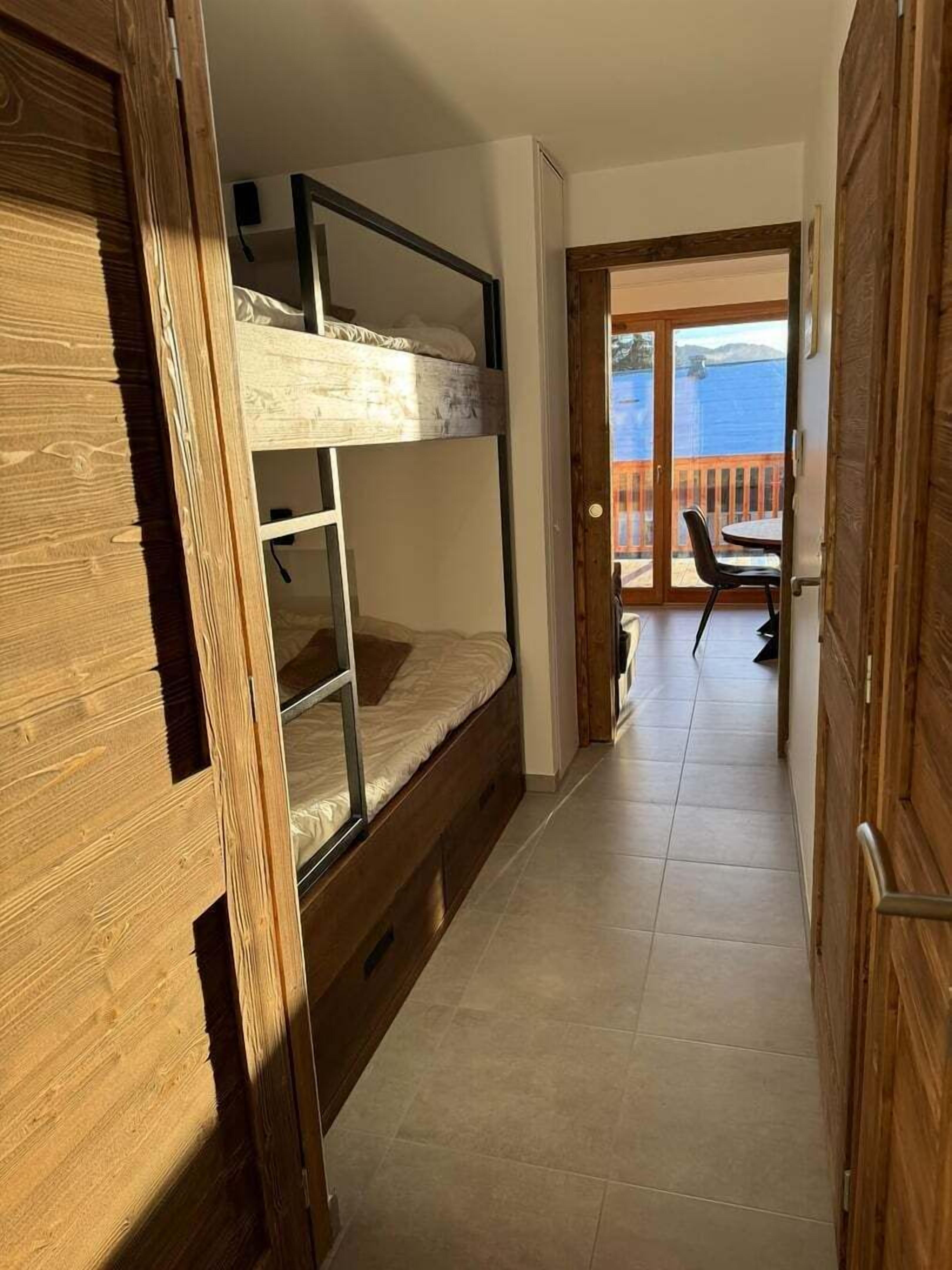 A room with a bunk bed, a small table, and a view of the sea through a glass door.
