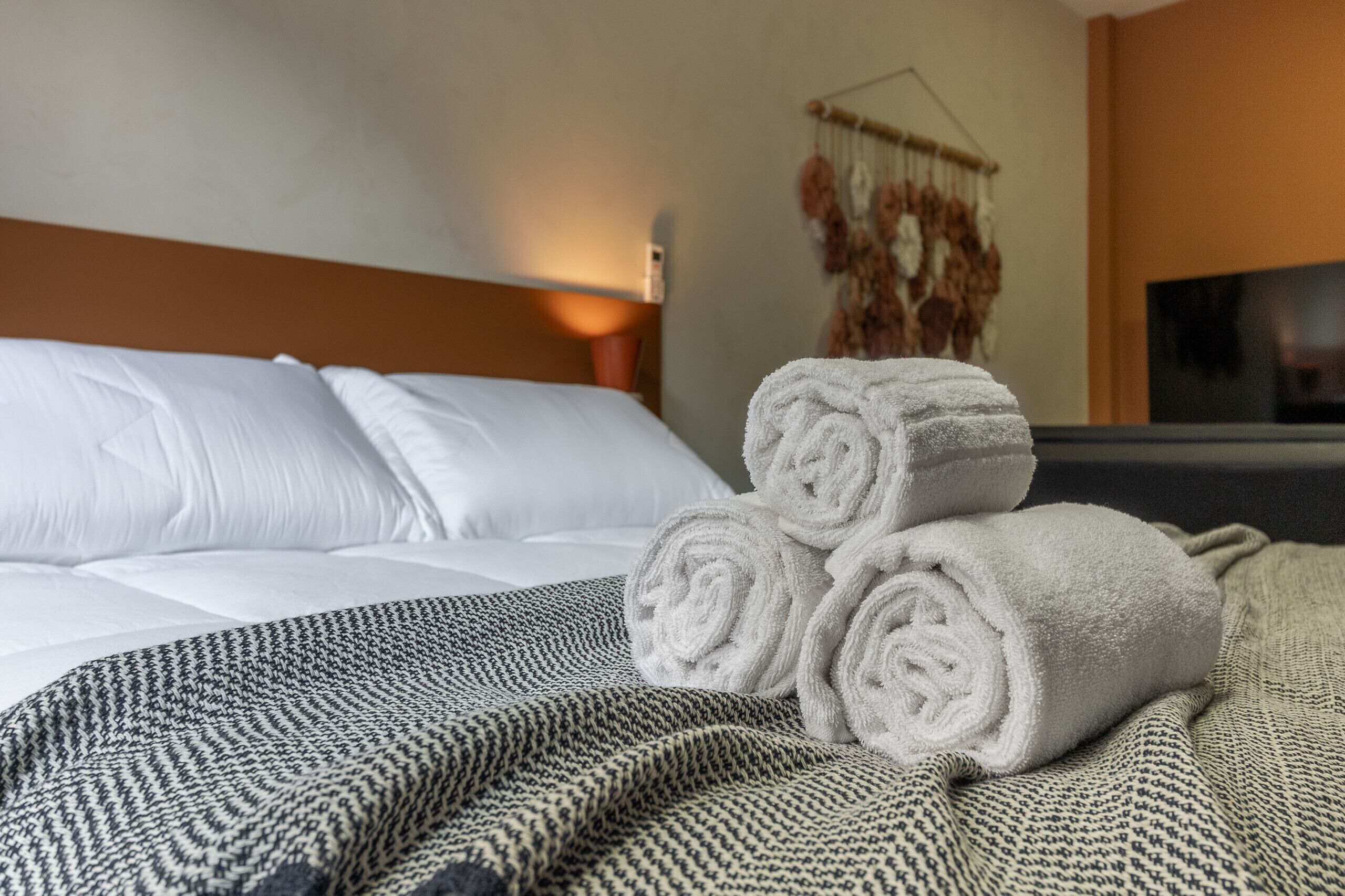 A neatly made bed with white linens, a patterned blanket, and rolled towels on a textured bedspread.
