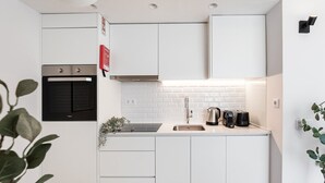 A compact kitchen with white cabinetry, a built-in oven, a stainless steel sink, and a coffee maker. - GuestReady - Porto's Modern Comfort (Porto)