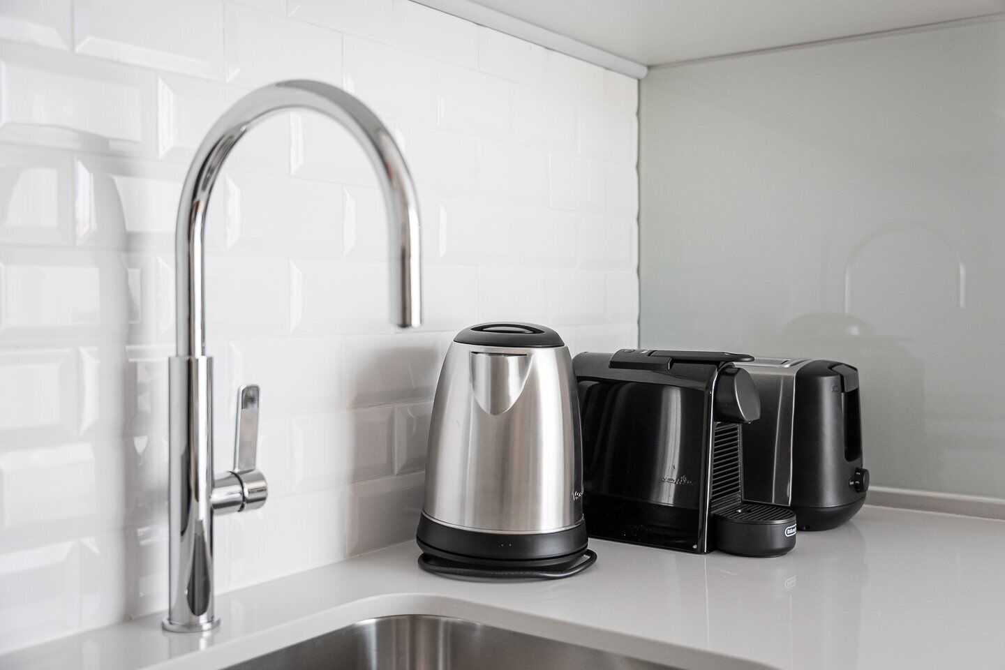 A kitchen with a stainless steel sink, a modern faucet, a kettle, and a coffee maker.