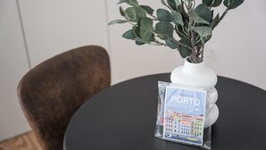A white vase with green leaves on a black table, next to a small booklet titled "Embrace Porto". - GuestReady - Porto's Modern Comfort (Porto)
