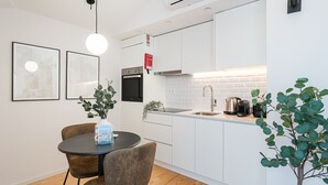 A modern kitchen with white cabinets, a stainless steel sink, and a built-in oven. There is a dining table with two chairs and a potted plant. - GuestReady - Porto's Modern Comfort (Porto)