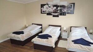 Une chambre d’hôtel avec trois lits simples, un plancher en bois et un mur orné de trois tableaux encadrés.
