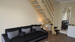 Un salon avec un canapé noir, un escalier en bois et un meuble blanc.