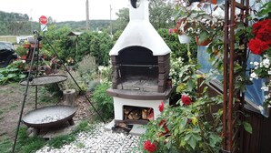 Un four à pizza rustique installé à l’extérieur, entouré d’un jardin agrémenté d’un panneau de signalisation, d’un pot de fleurs suspendu et d’une clôture en bois.