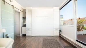 Een moderne, compacte kamer met een schuifdeurkast, een glazen scheidingswand en een groot raam met uitzicht.