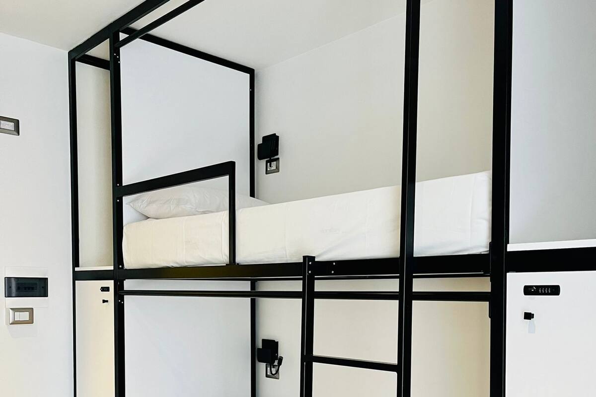 A bunk bed room with a black metal frame, white bedding, and a wall-mounted light fixture.