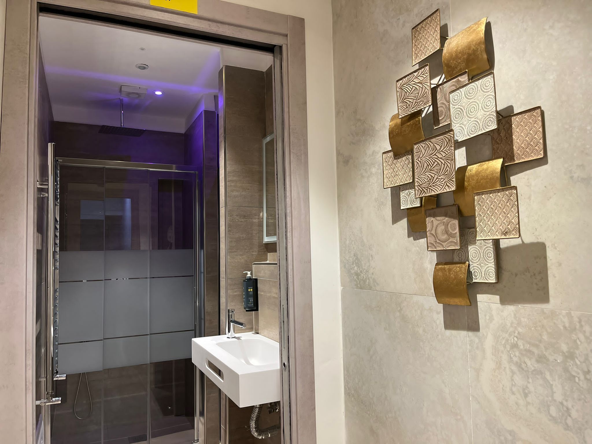 Un bagno moderno con cabina doccia in vetro, un lavandino bianco e pannelli decorativi alle pareti.