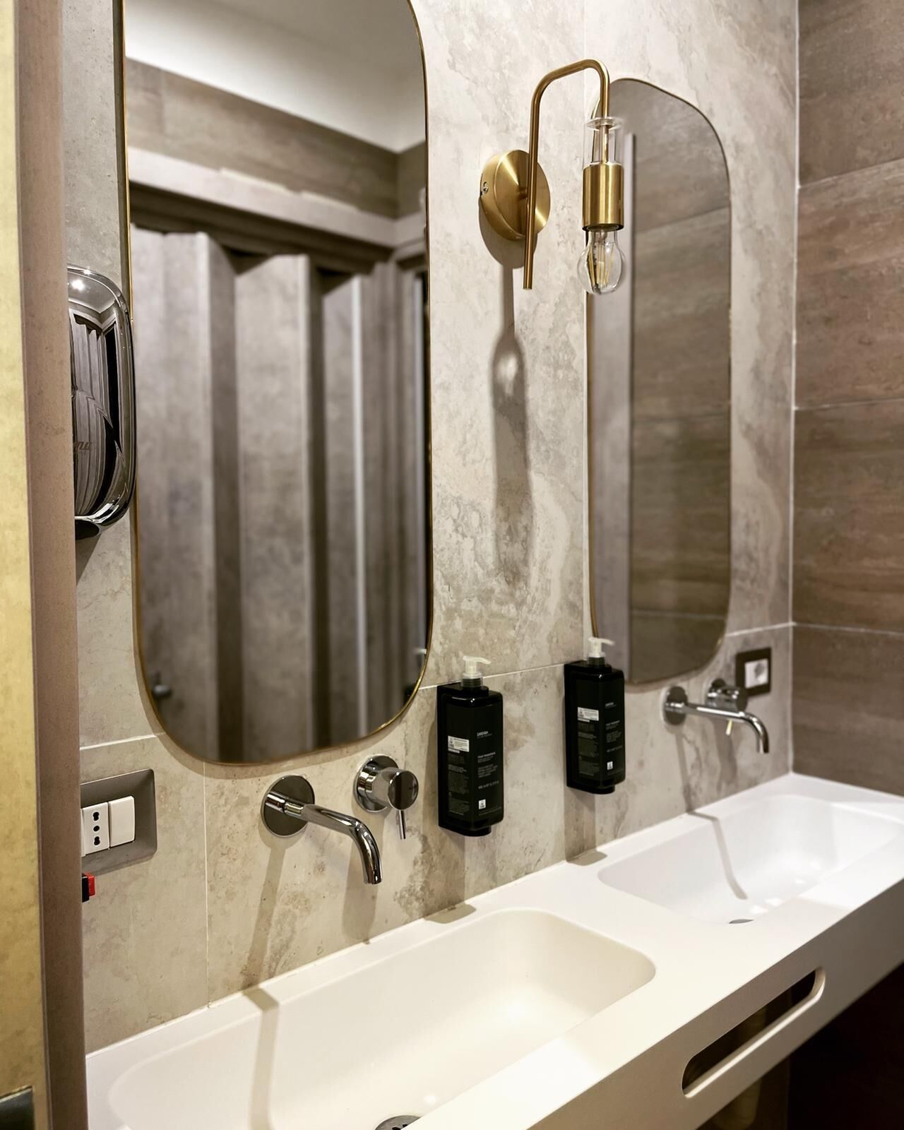 A modern bathroom with two sinks, a mirror, and a towel dispenser.