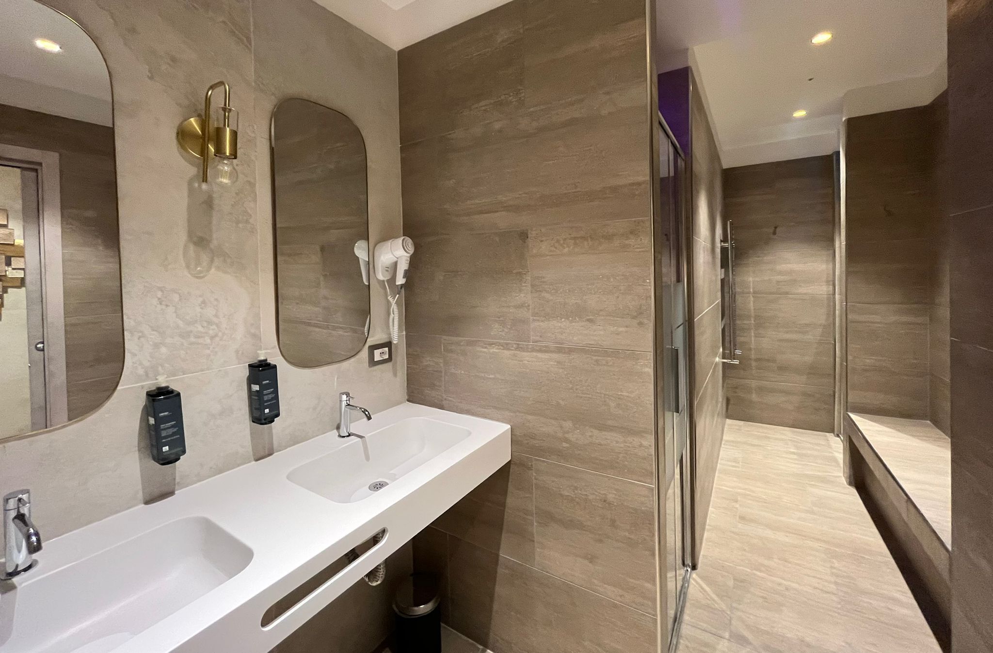 Une salle de bain moderne avec deux lavabos, un grand miroir, une douche à parois de verre et des toilettes.
