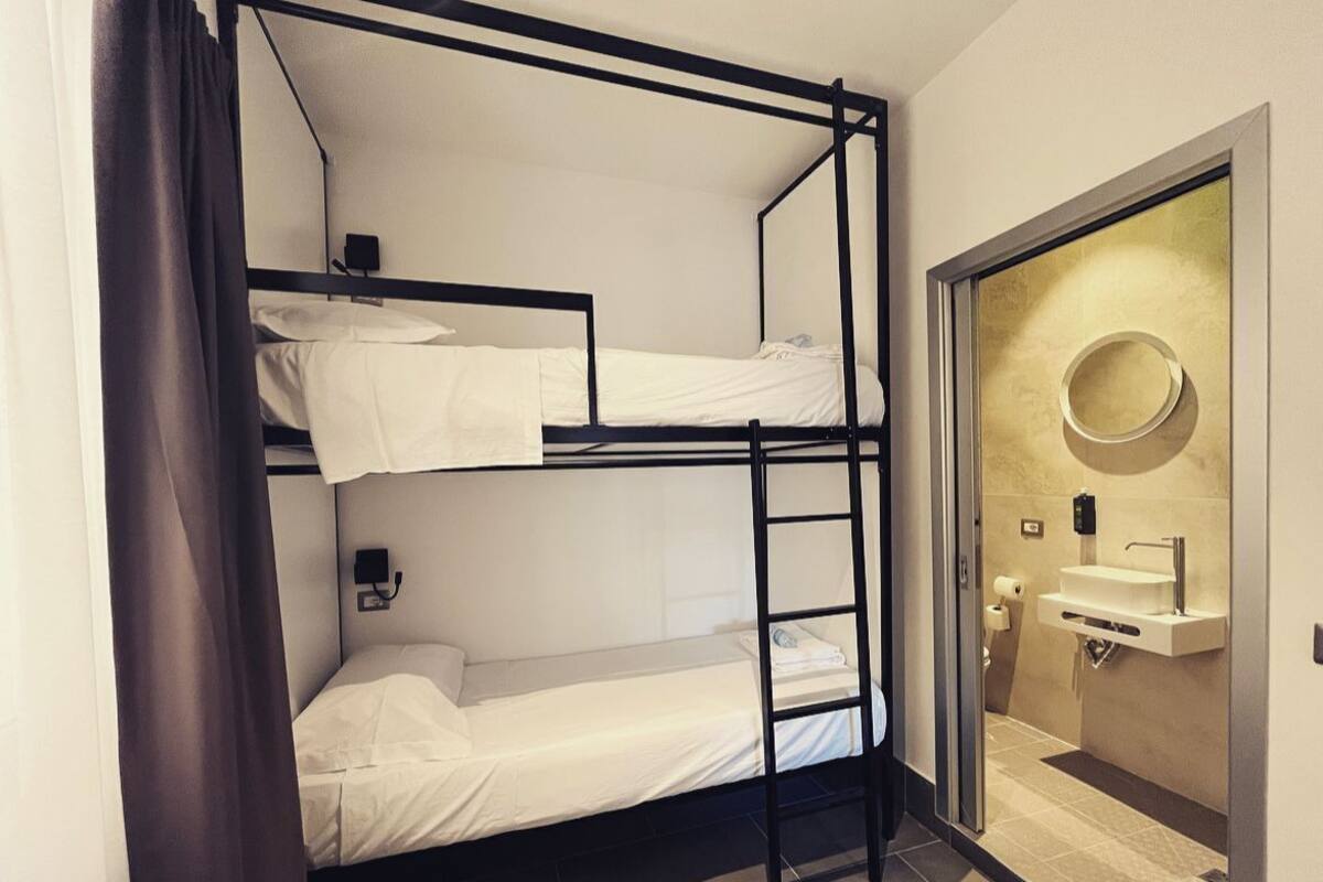 A bunk bed room with a ladder, a wall-mounted light, and a bathroom with a sink and mirror.
