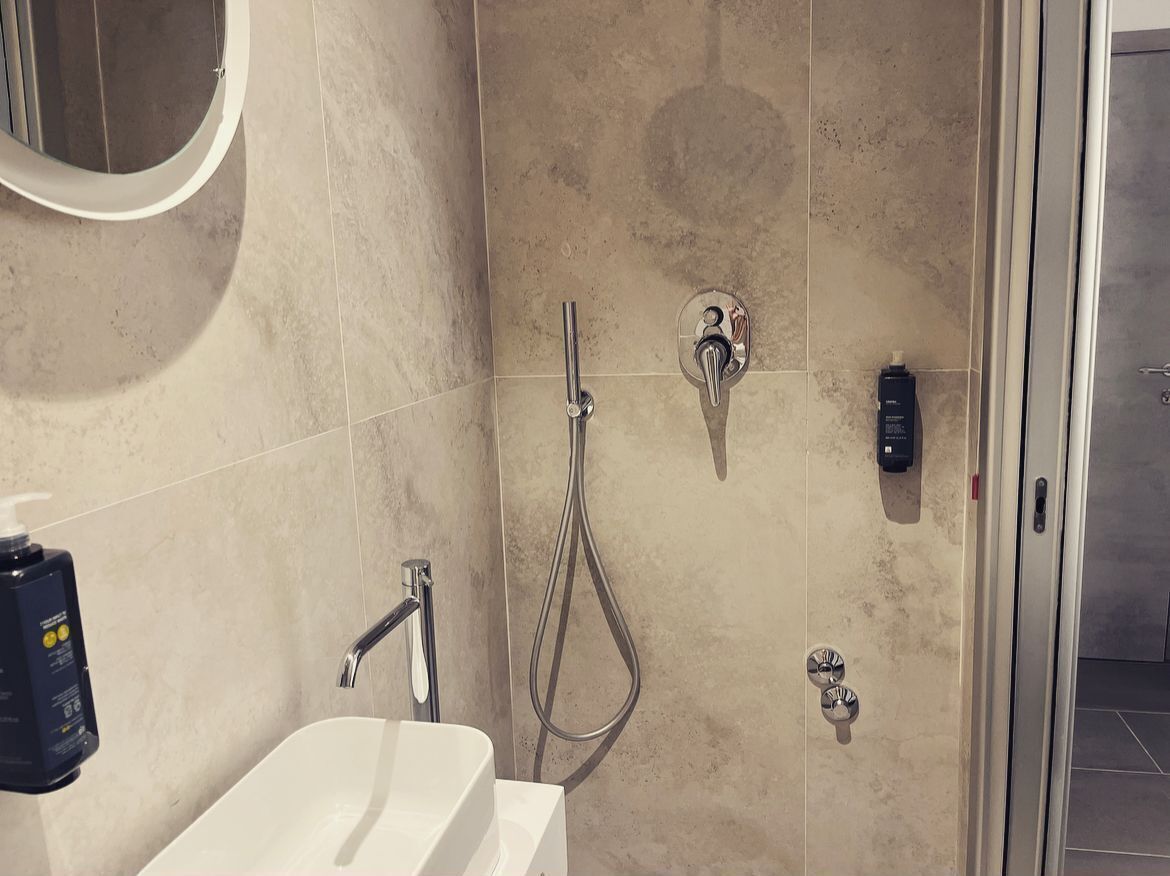 A bathroom with a white sink, a handheld showerhead, and a wall-mounted faucet.