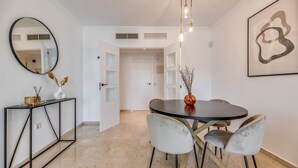 A dining area with a round table, four chairs, a vase with dried flowers, a black console table with a mirror, and a framed abstract artwork on the wall. - Puerto Banus Serenity Retreat (Marbella)