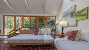 Ein Schlafzimmer mit zwei Betten, einem großen Fenster, einem roten Teppich mit Muster und einem Gemälde an der Wand.
