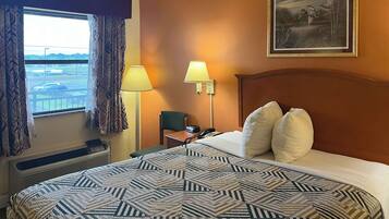 A hotel room with a large bed, two bedside lamps, a painting on the wall, and a view of the airport through the window.