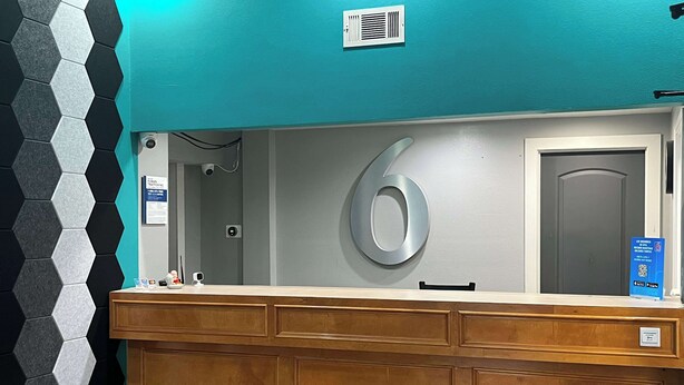 A reception desk with a teal wall, a number '6' sign, and a blue informational sign. - Motel 6 Morrilton, AR (Morrilton)