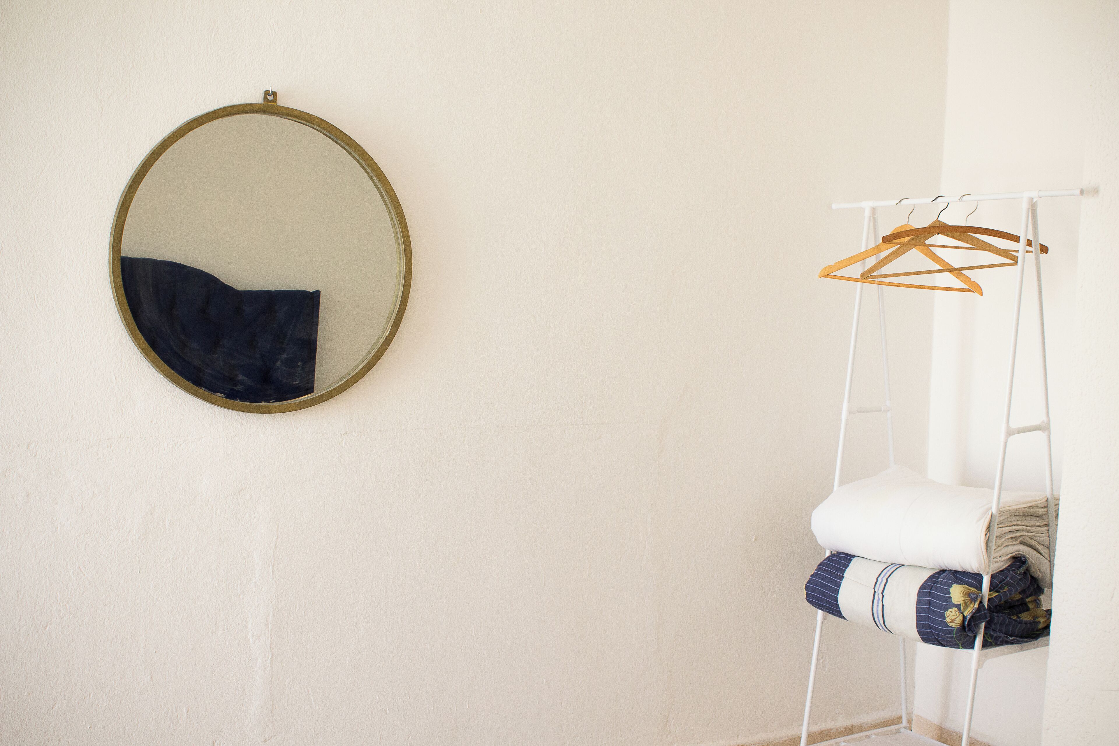 Une pièce avec un grand miroir rond au mur, un mur blanc et une chaise suspendue blanche sur laquelle sont posés des vêtements.