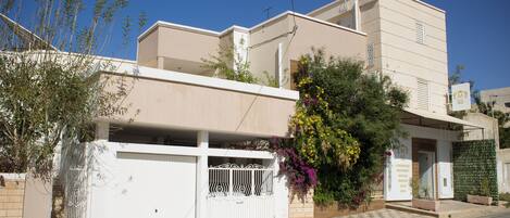 Un edificio moderno de dos pisos con fachada blanca, entrada protegida por una reja y un pequeño balcón.