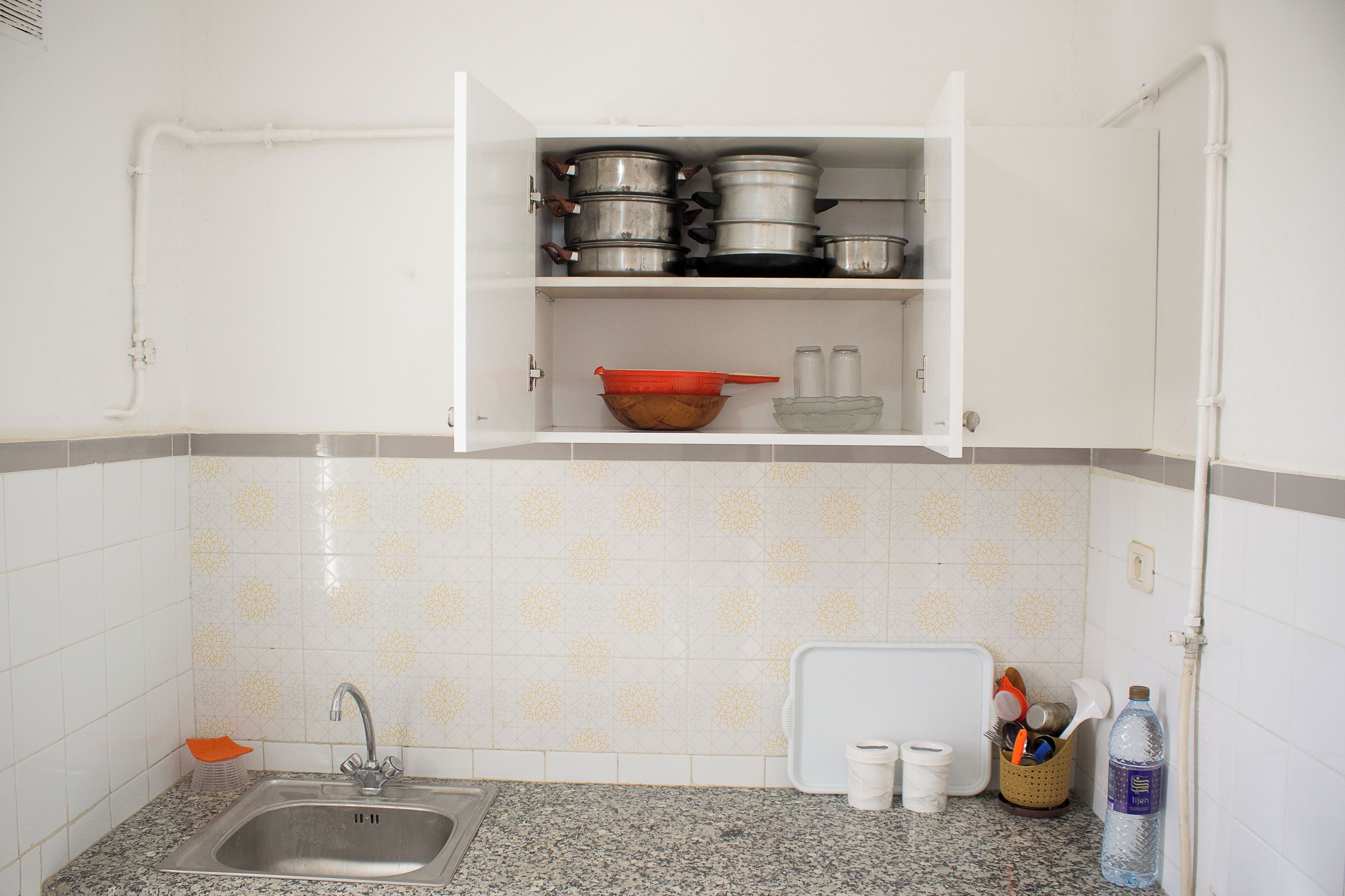 A kitchen with a granite countertop, stainless steel sink, white cabinets, and patterned backsplash.
