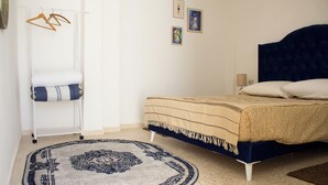 A bedroom with a bed, a hanging clothes rack, a small rug, and two framed pictures on the wall.