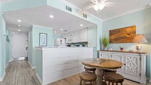 A kitchen with a central island, white cabinetry, and a dining area with stools. - Oceanfront Delight - Indoor Pool, Sleeps 4 (North Myrtle Beach)
