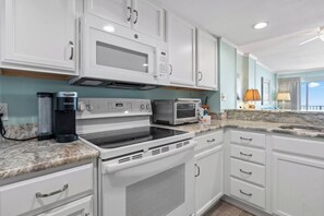 A modern kitchen with white cabinetry, a built-in microwave, a Keurig coffee maker, a stovetop oven, and a toaster. - Oceanfront Delight - Indoor Pool, Sleeps 4 (North Myrtle Beach)