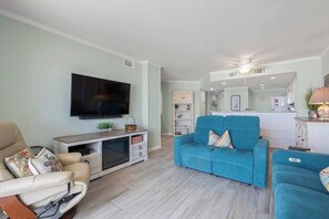 A living room with a flat-screen TV, a blue sofa, and a beige armchair. - Oceanfront Delight - Indoor Pool, Sleeps 4 (North Myrtle Beach)