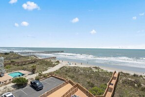 Une plage avec vue sur une jetée, une piscine et un espace de stationnement.