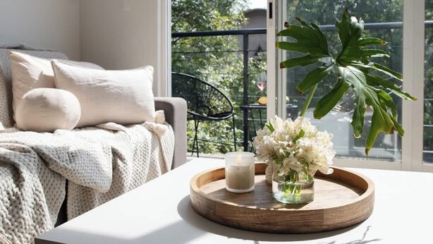 Et værelse med en hvid sofa, en træbakke med et lys og blomster, samt en stor plante.