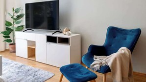 En moderne stue med et fladskærms-tv på et hvidt skab, en blå lænestol, en lille skammel og en potteplante.