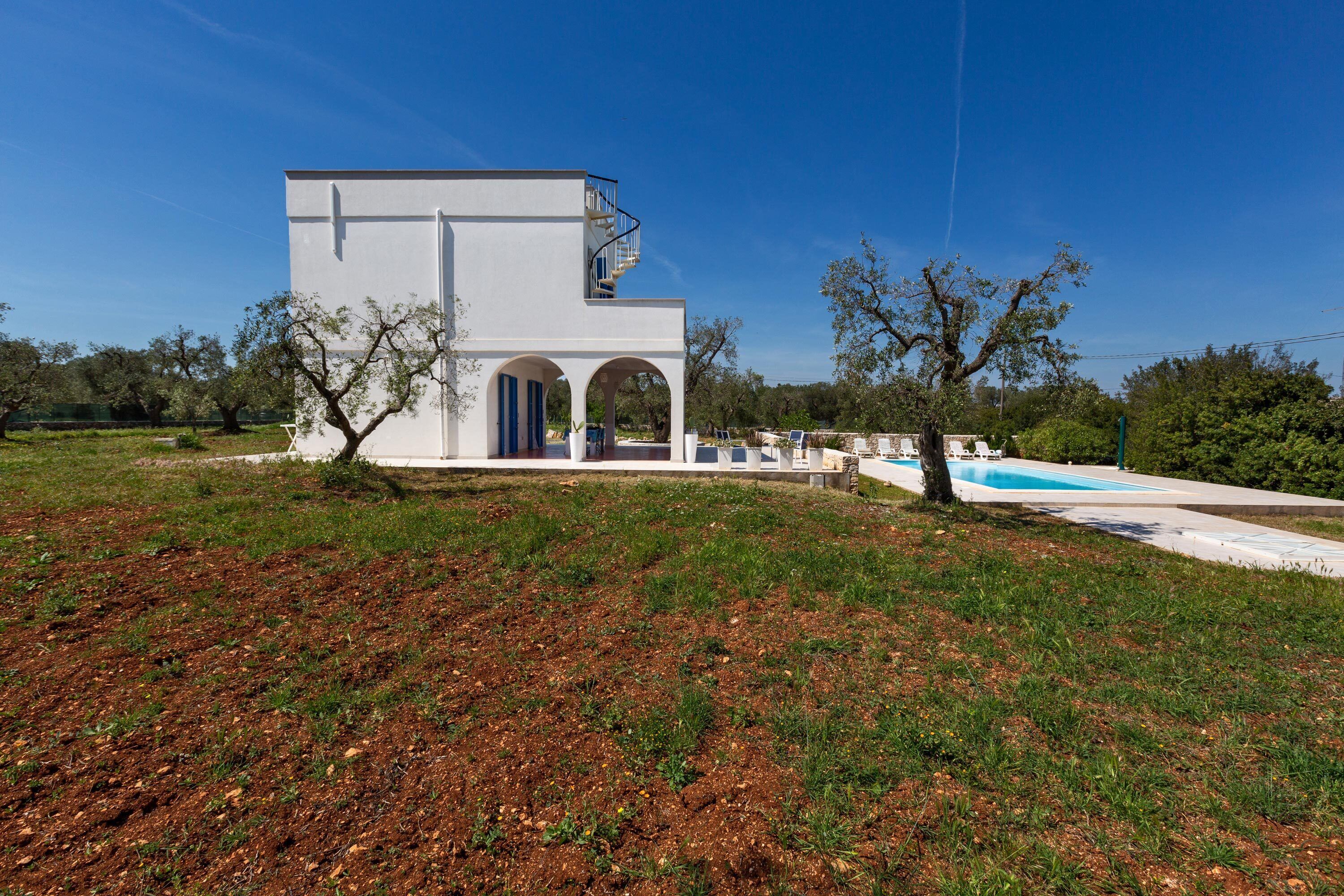 A modern white building with a pool, surrounded by trees and a clear sky.