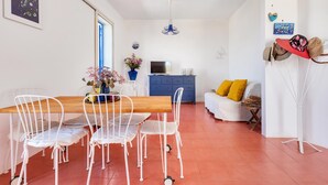 A dining area with a wooden table and white chairs, a blue cabinet, a TV, and a sofa with yellow cushions. - 3880 Villa Sierri by Perle di Puglia (Carovigno)