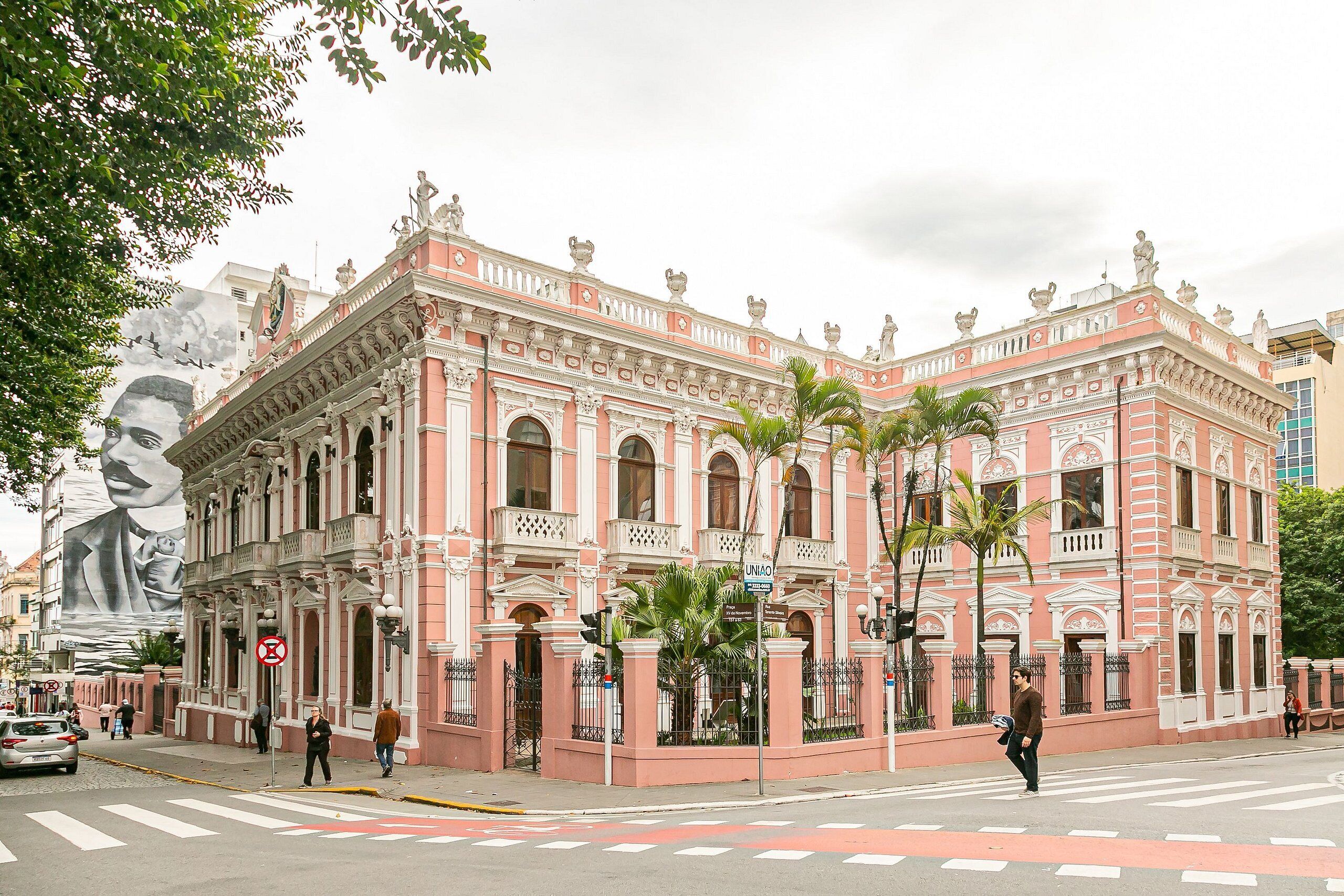 Un edificio rosa de arquitectura clásica, con columnas y estatuas, situado en una esquina.