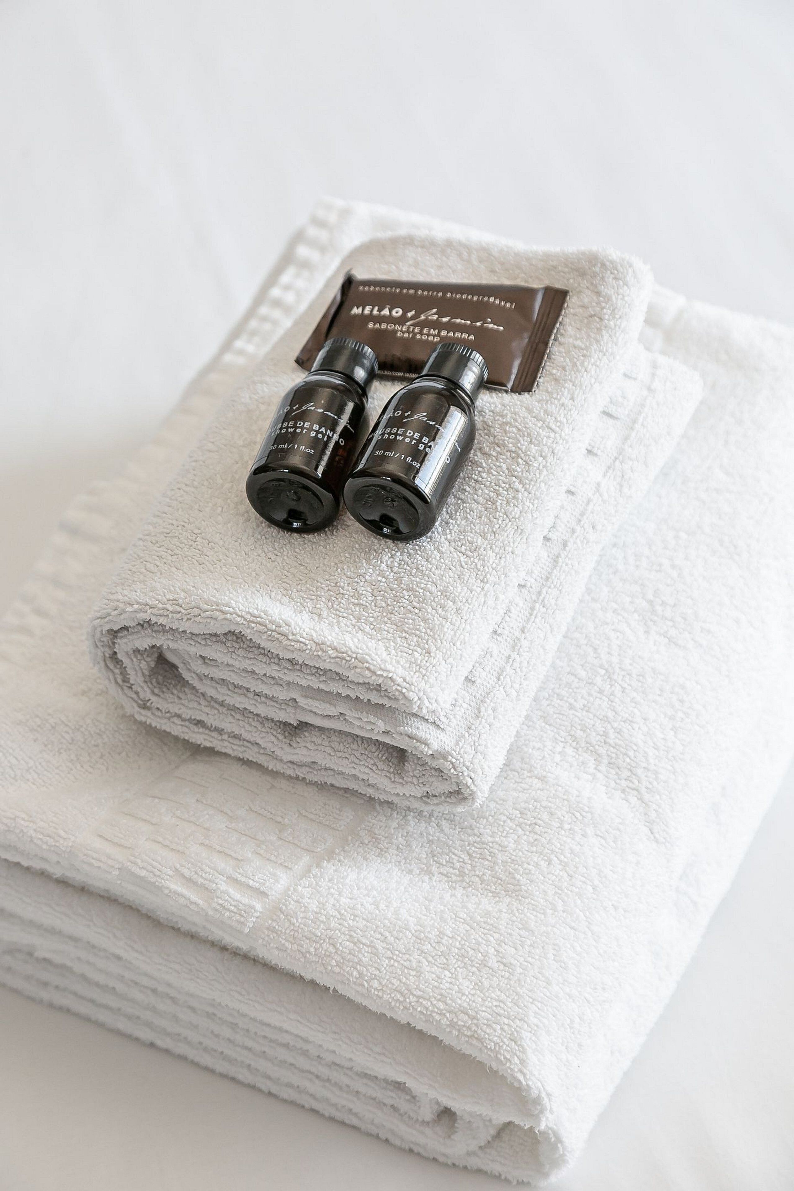 A neatly folded white towel with two small bottles of shower gel and a bar soap on top.