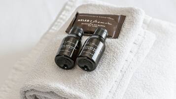 A neatly folded white towel with two small bottles of shower gel and a bar soap on top.
