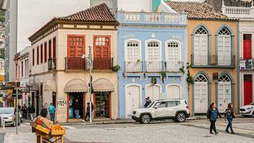 A street with colorful buildings, a white car parked on the side, and a fruit stand.
