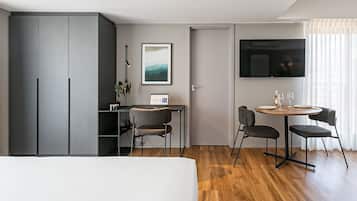 A modern hotel room with a bed, a desk with a chair, a TV, and a dining area with chairs and a table.