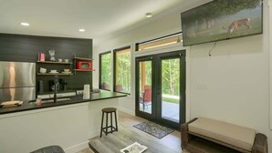 A modern kitchen with a large refrigerator, microwave, and sink. There is a bar area with stools, a seating area with a bench, and a large window offering a view of the outdoors. - Love Shack cabin at Trickle Creek (Logan)