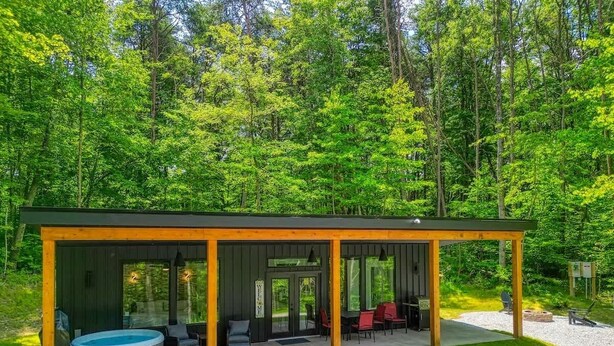 A covered outdoor area with a hot tub, seating, and a wooden deck. - Love Shack cabin at Trickle Creek (Logan)