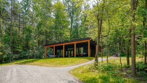A modern building with a covered porch, surrounded by a forest. - Love Shack cabin at Trickle Creek (Logan)