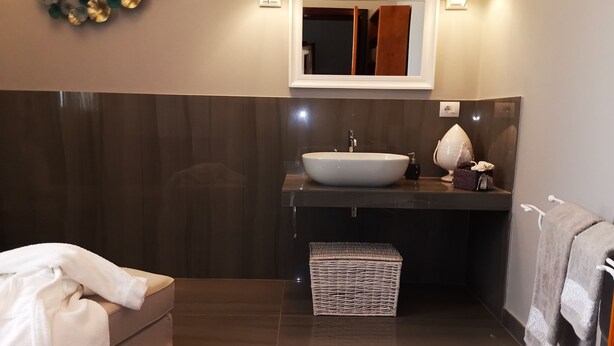 A modern bathroom with a large white sink, dark wood paneling, a mirror above the sink, and a wicker basket below it.
