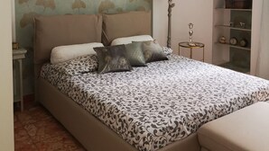 A bedroom with a bed, pillows, a nightstand, a lamp, and a shelf with items.